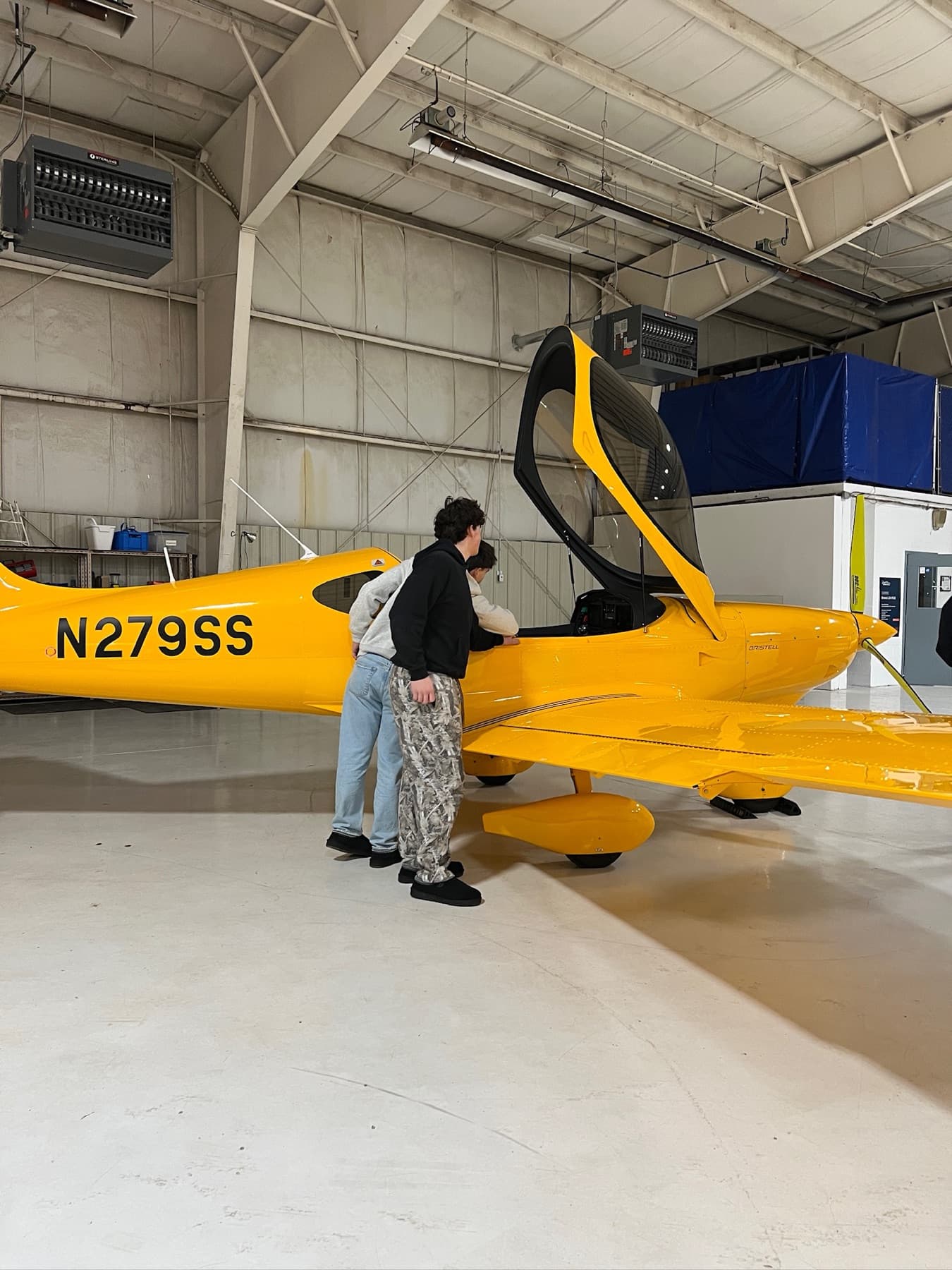 Students looking into the open cockpit of a yellow Bristell in the hangar