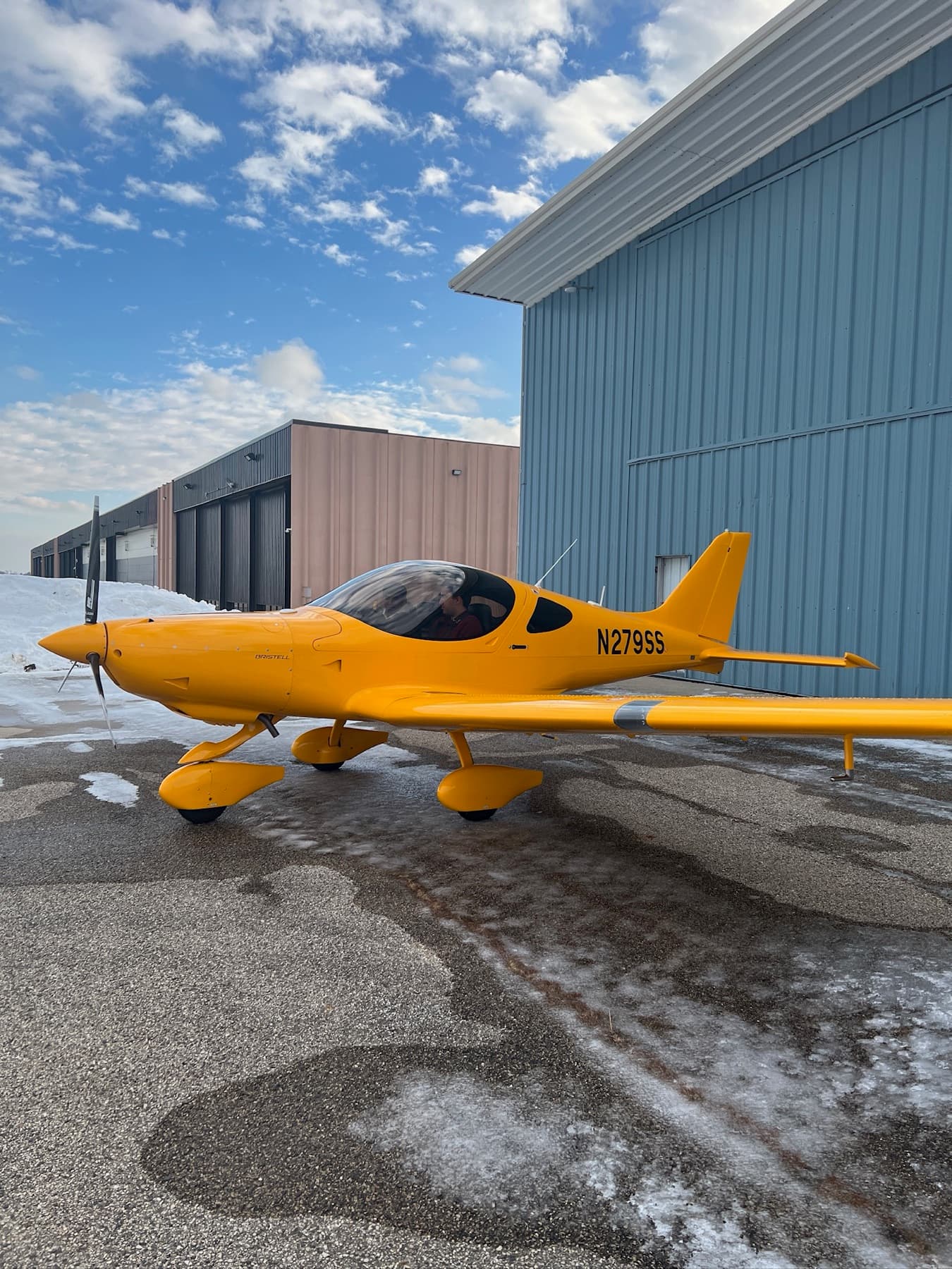 A yellow Bristell parked outside the hangar under a clear sky