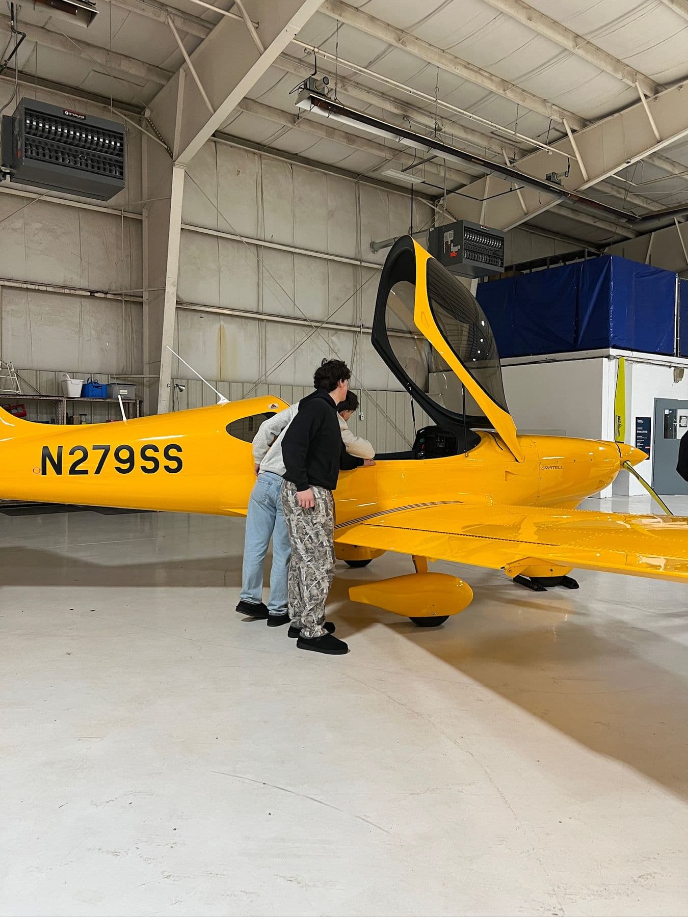 Students at the open canopy of the yellow Bristell N279SS in the hangar