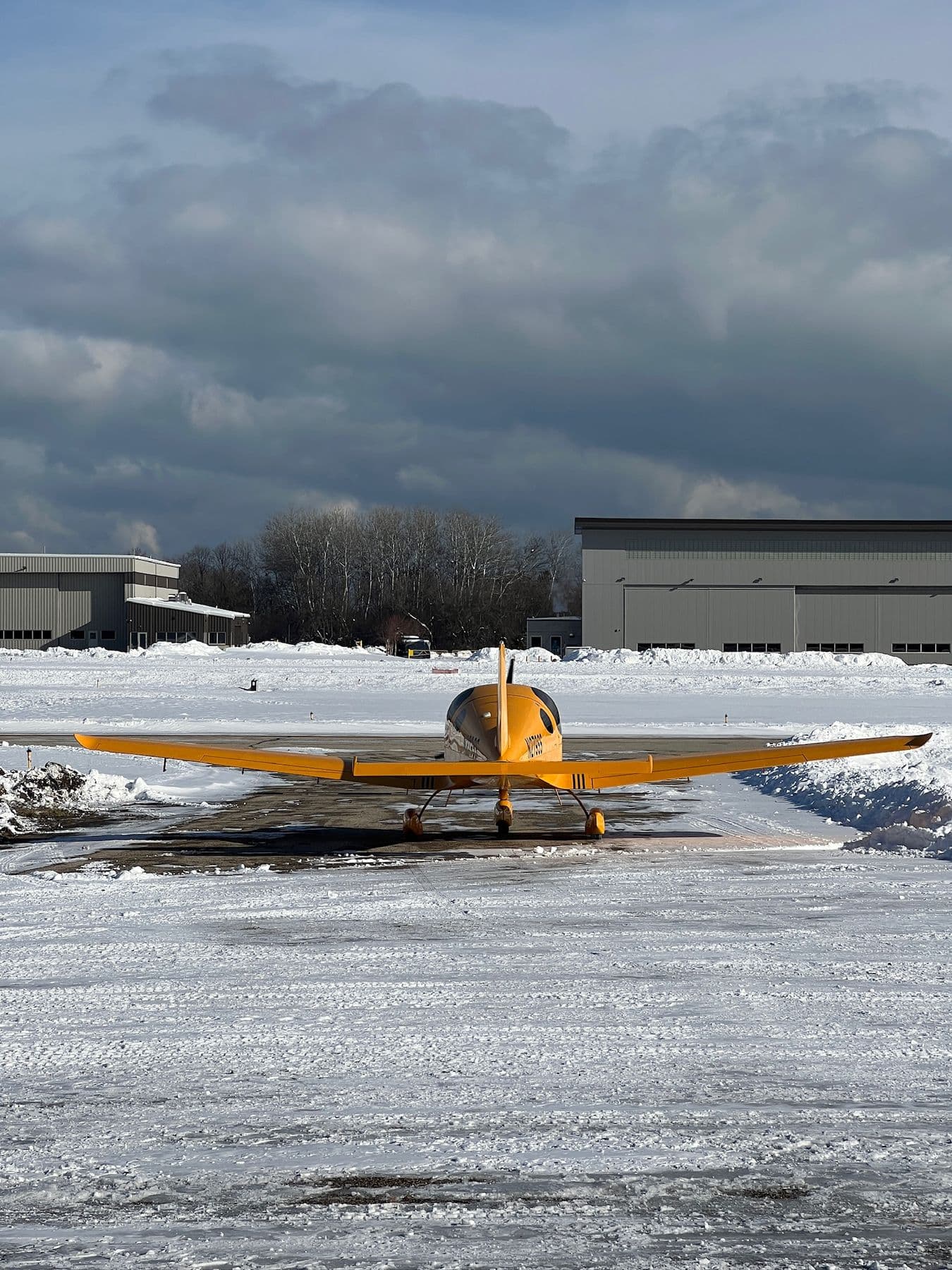 A yellow Bristell on the ramp in front of the hangars