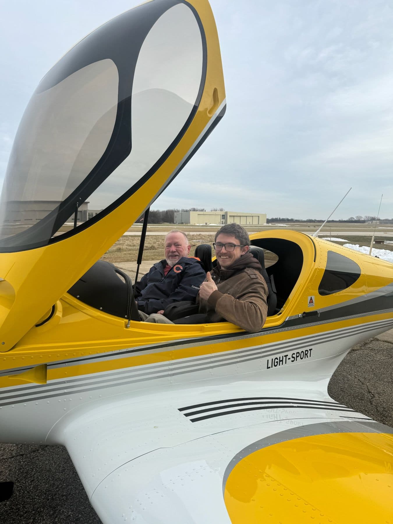 Two pilots seated in the cockpit of a yellow Bristell