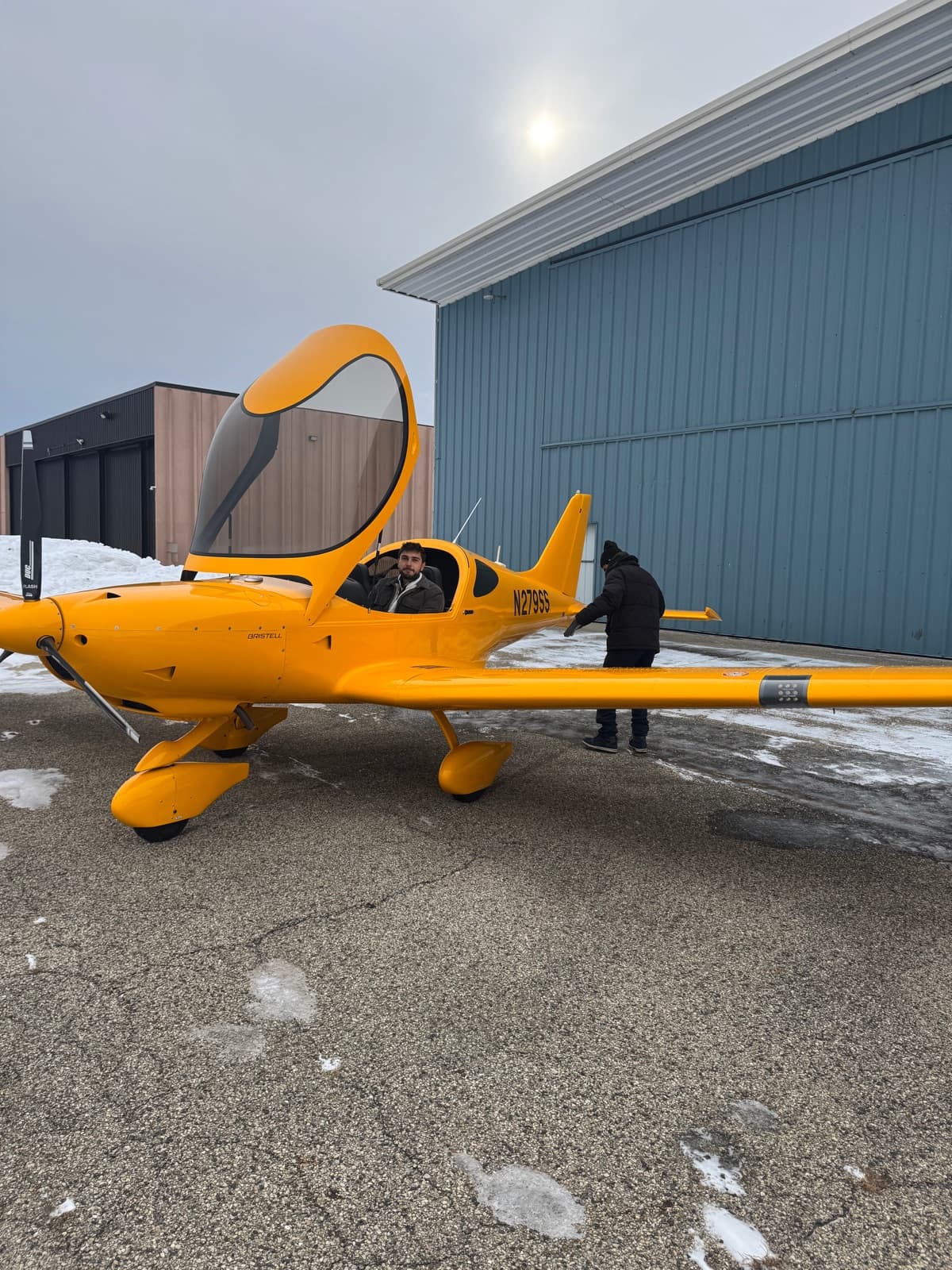 A student walking out to a yellow Bristell on the ramp in low winter sun